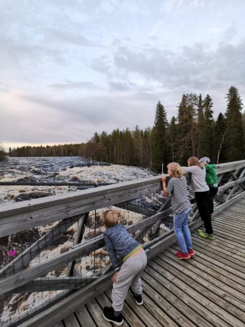 Lapset katselevat sillan kaiteen yli kuohuvaa jokea.